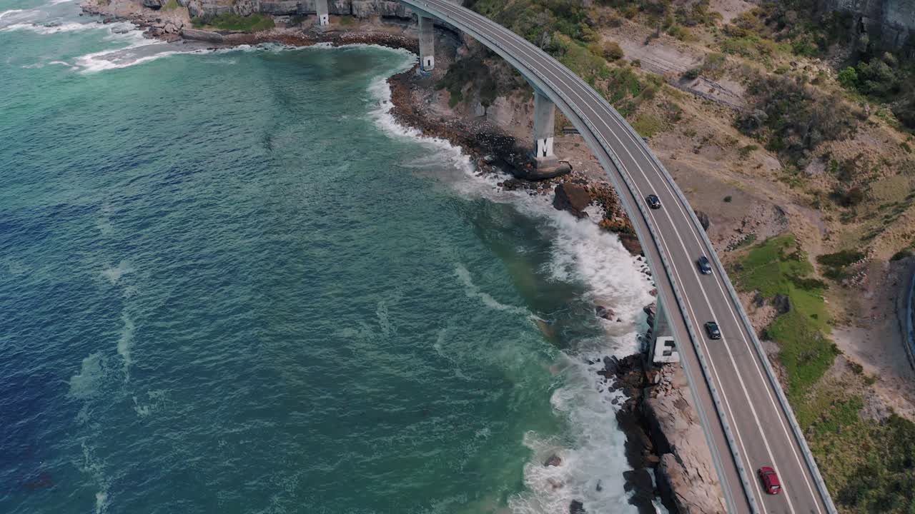 vehículos que circulan en el puente del acantilado marino con olas rompientes en nueva gales del sur, australia