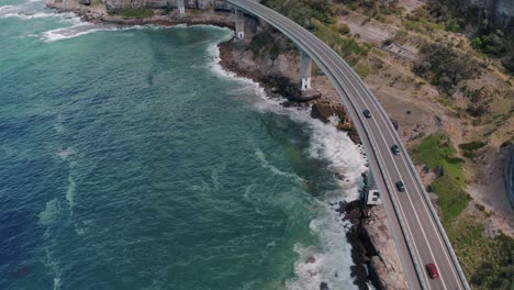 Vehículos-Que-Circulan-En-El-Puente-Del-Acantilado-Marino-Con-Olas-Rompientes-En-Nueva-Gales-Del-Sur,-Australia