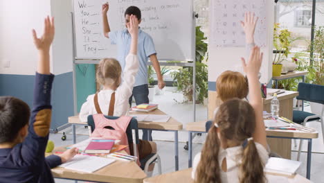 estudiante parado frente a la pizarra en el aula de inglés elige a un compañero de clase pelirrojo que tiene el brazo levantado 1