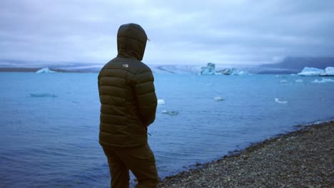 Hombre-Paseando-Por-La-Orilla-De-La-Laguna-Glaciar-Jokulsarlon-Con-Pequeños-Icebergs-Flotantes-En-Islandia