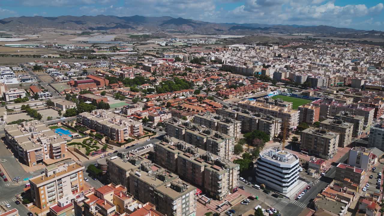 Aerial view of the urban districts of Águilas in the Murcia region of Spain, showing residential blocks, streets, and coastal areas framed by surrounding hills and countryside