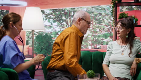 Medical-assistant-consulting-elderly-man-with-a-stethoscope-during-home-visit