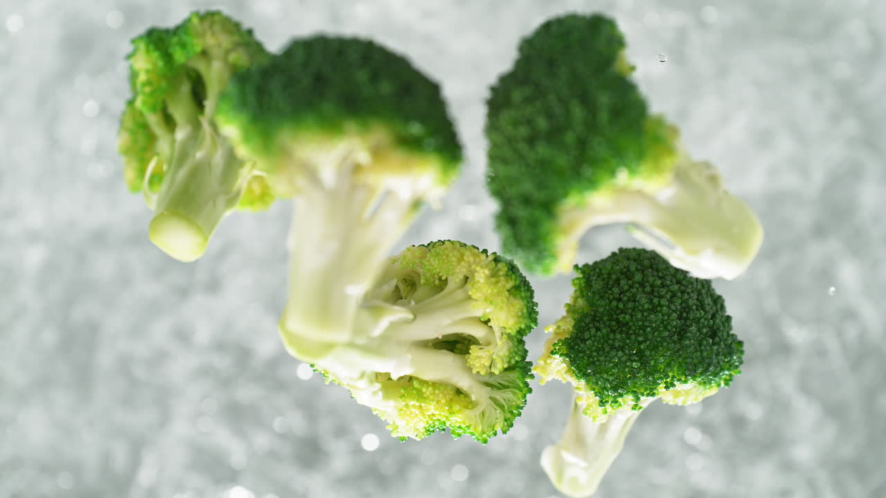 Broccoli Florets Falling Into Pot Of Boiling Water Making a Splash In Slow Motion, Table Top View