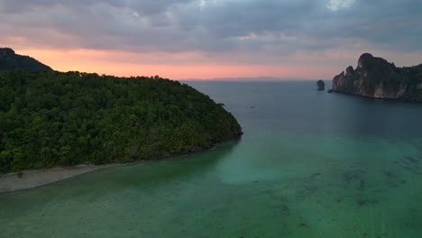 Atemberaubender-Luftblickflug-über-Eine-Tropische-Insel-Bei-Sonnenuntergang-Und-Wolkigem-Himmel-Mit-Booten,-Die-Auf-Einem-Türkisfarbenen-Meer-Segeln