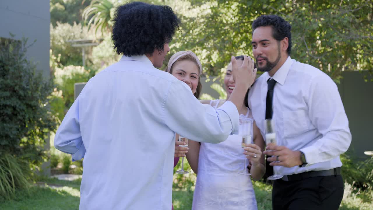 Amici diversi che brindano in giardino dopo che una donna in bianco alza le braccia ed esulta, passando una bottiglia.