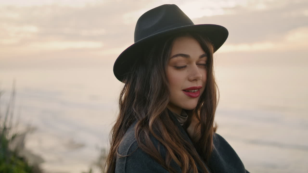 Romantic brunette smiling camera at seashore with cloudy sky backdrop close up.