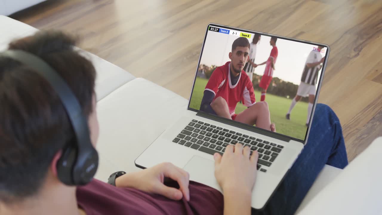 adolescente caucásico usando una computadora portátil con varios jugadores de fútbol masculino jugando un partido en la pantalla