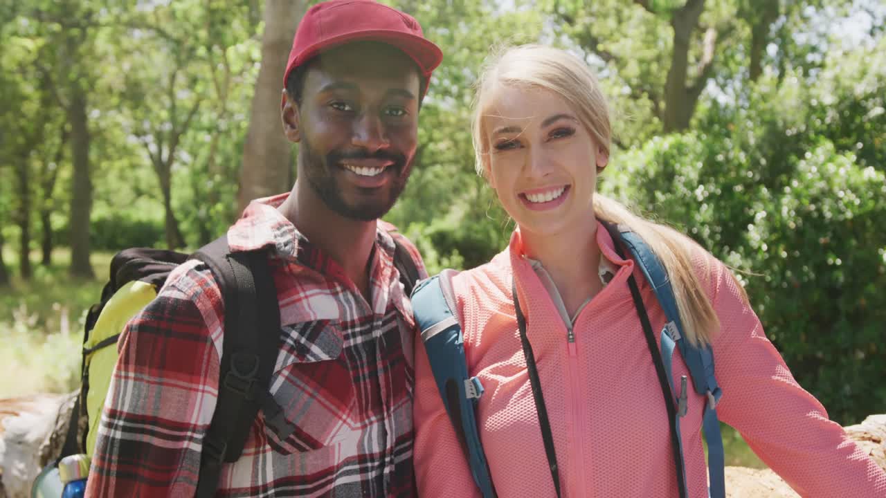 retrato de una feliz pareja diversa con mochilas abrazándose en el parque, cámara lenta