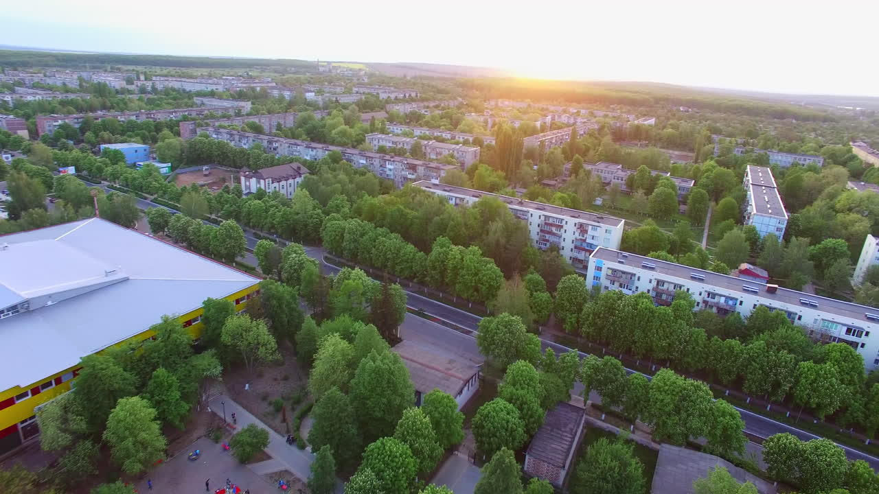 Setting sun over the beautiful green city. Green residential area with multi-storied buildings and private houses. Top view.