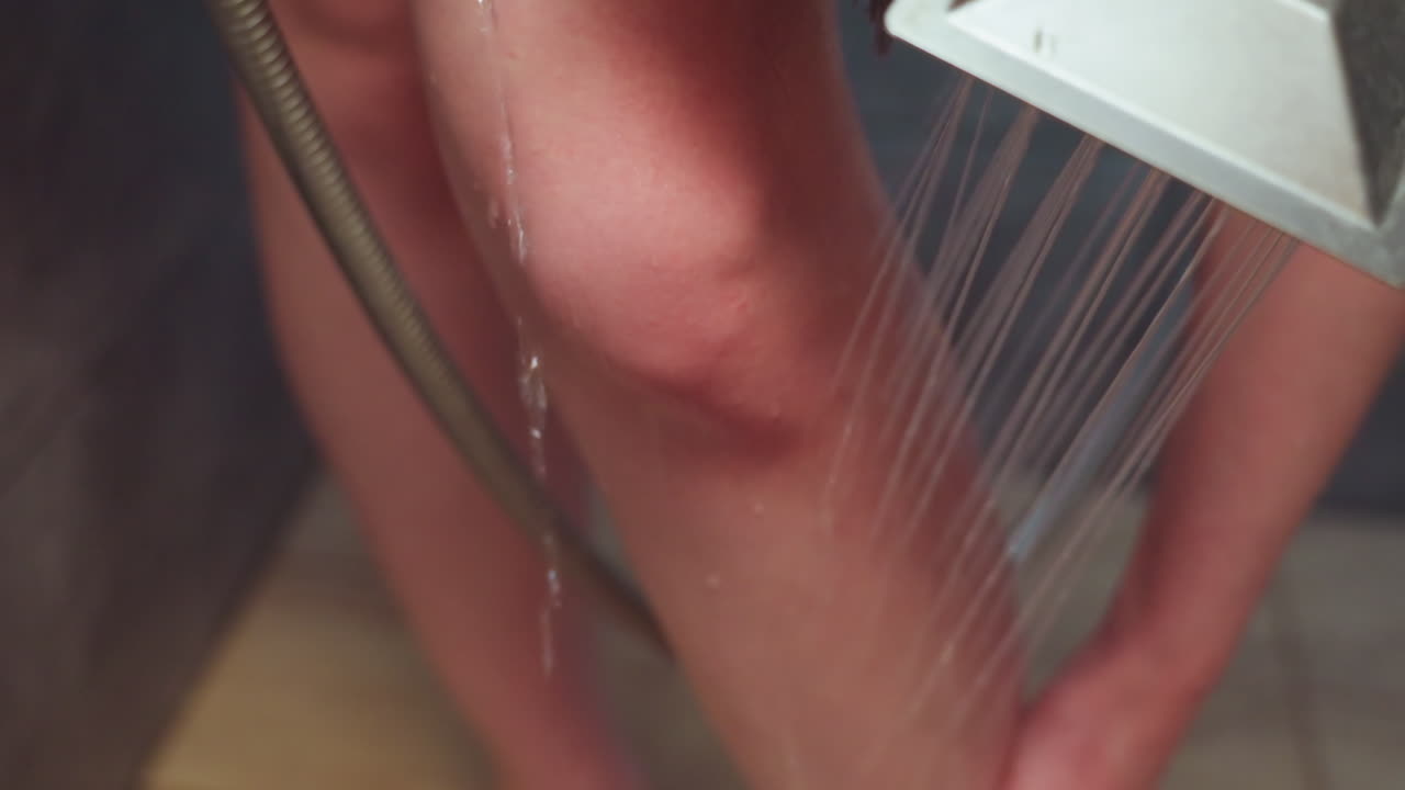 close up of adult woman washing leg with handheld shower stream, water cascading down smooth skin, capturing peaceful moment of personal hygiene, bath ritual