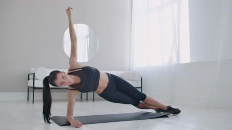 the brunette in the apartment does an exercise plank while standing in a static position on the lateral muscles of the abs and moving her hand up and down