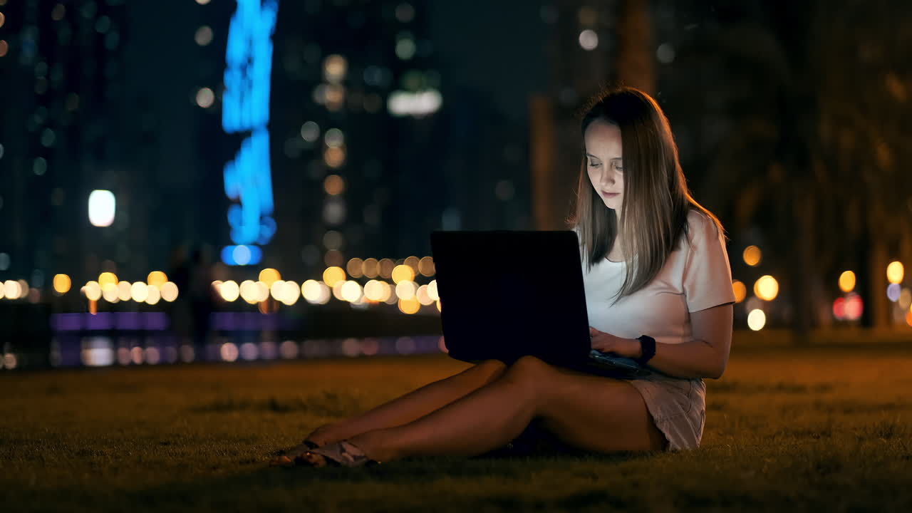 una joven estudiante con una computadora portátil por la noche en la ciudad mirando la pantalla de la computadora y escribiendo con las manos en el teclado. trabajo remoto en internet. la estudiante hace el trabajo. vida nocturna en la ciudad