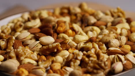 close up shot of nuts falling into bowl containing cashews dry roasted peanuts pistachio walnuts and hazelnuts 1