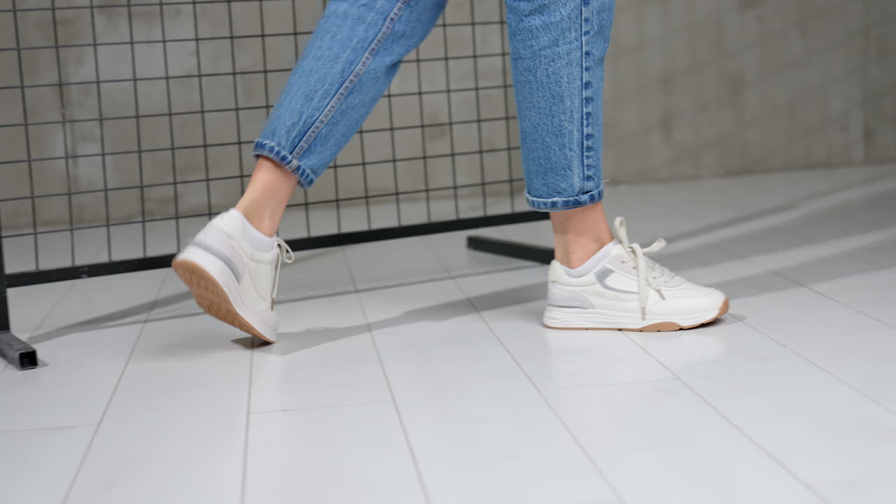 Girl in short blue jeans and light white sneakers. Trendy sport shoes presentation in photo studio.
