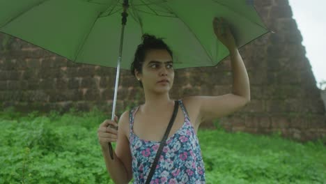 mujer joven sosteniendo un paraguas en un entorno al aire libre verde exuberante en un día de lluvia
