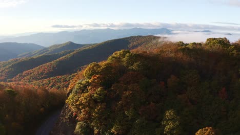 aerial view of the blue ridge parkway road between the colorful fall mountains with the peaks covered in fog and clouds at sunset