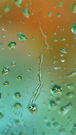 raindrops on blur colorful background. large drops flowing on glass window slowly in rainy weather. close-up. vertical video