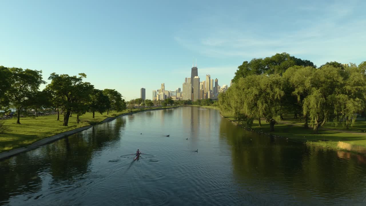 Drone Tracking Person Rowing in Water with Chicago Skyline in Background During Warm Summer Day