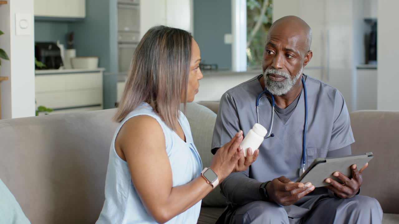 Mature woman holding pill bottle showing label, senior African American man checking tablet on sofa