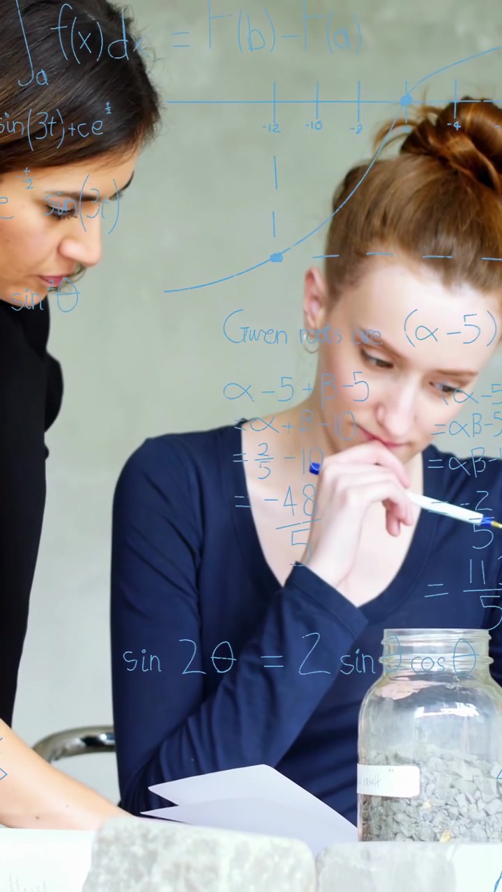 Vertical video: Sitting bun woman writing, peer leaning causing math overlay marking jar rocks lab