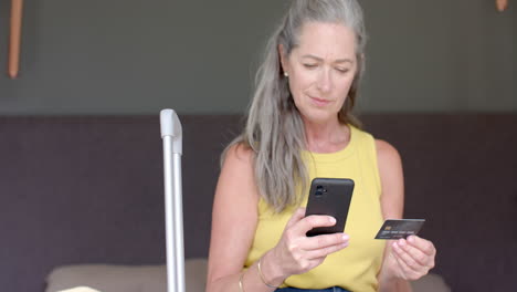 mujer caucásica madura con tarjeta de crédito, mirando su teléfono inteligente