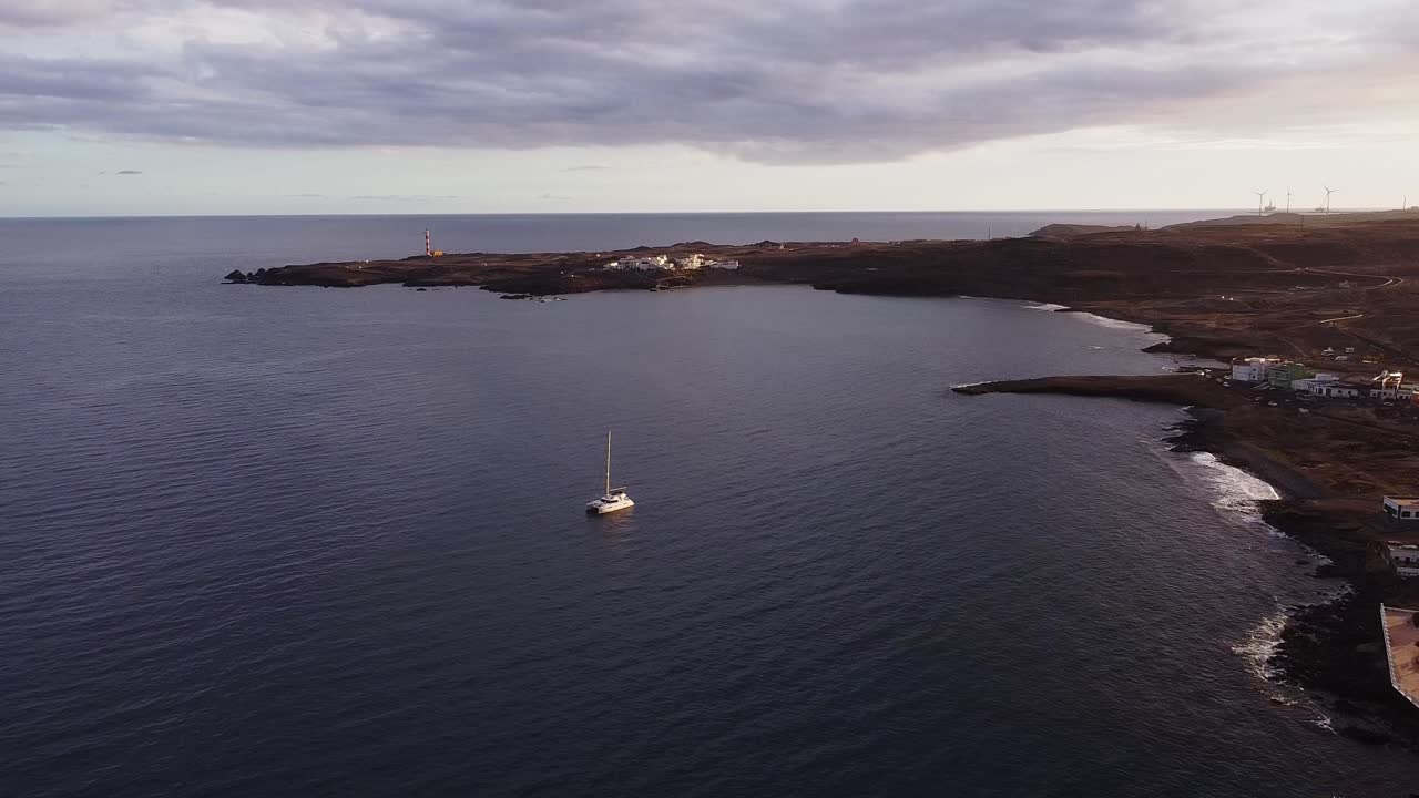 pintoresco aero, ciudad con casas y molinos de viento en la costa playa de la isla de tenerife durante la hora dorada de la noche sol de verano, barco de vela en el océano