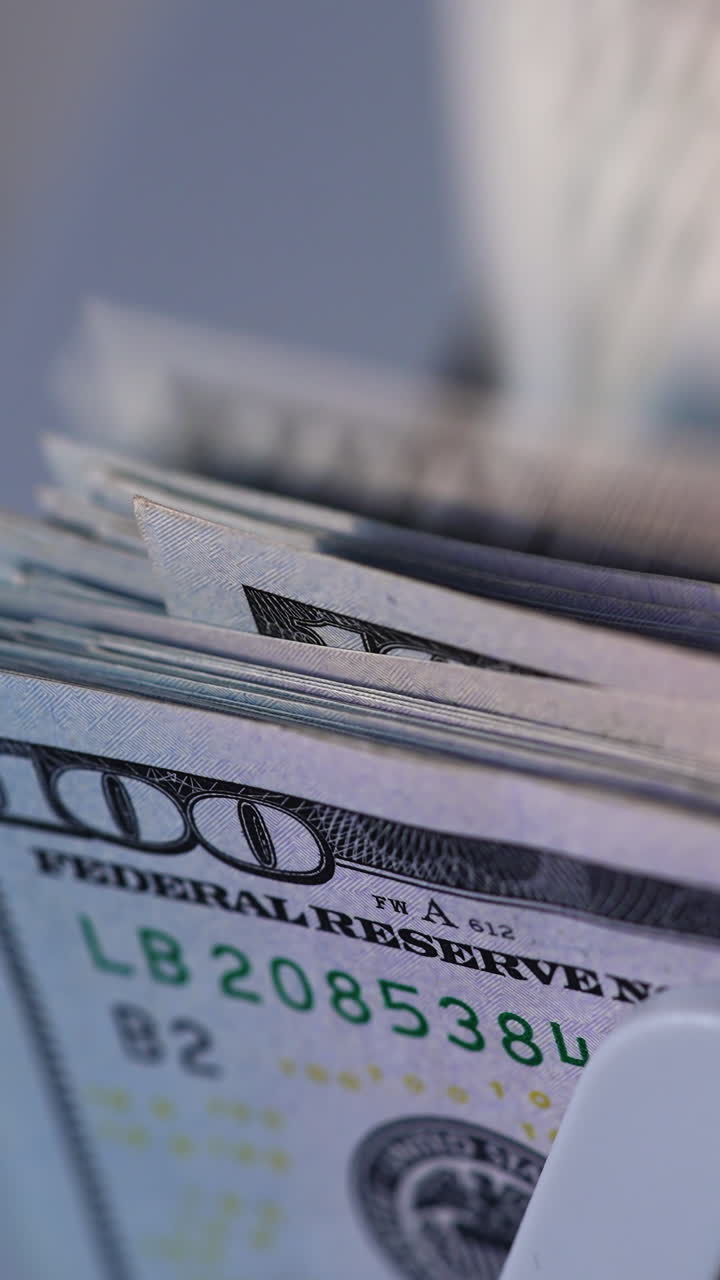 American currency hundred dollar bills falling on the holder of device. Close up. Money in cash counter machine. Vertical video