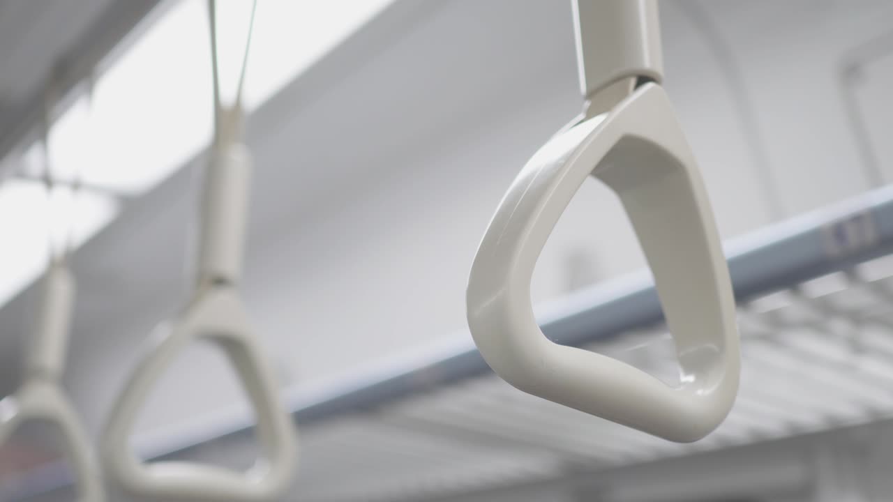 The hand ring  in the train carriage. The train is moving and the camera shakes slightly. The focus is on the front.  Look up. There are lights in the background.
