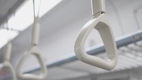 the hand ring  in the train carriage. the train is moving and the camera shakes slightly. the focus is on the front.  look up. there are lights in the background.