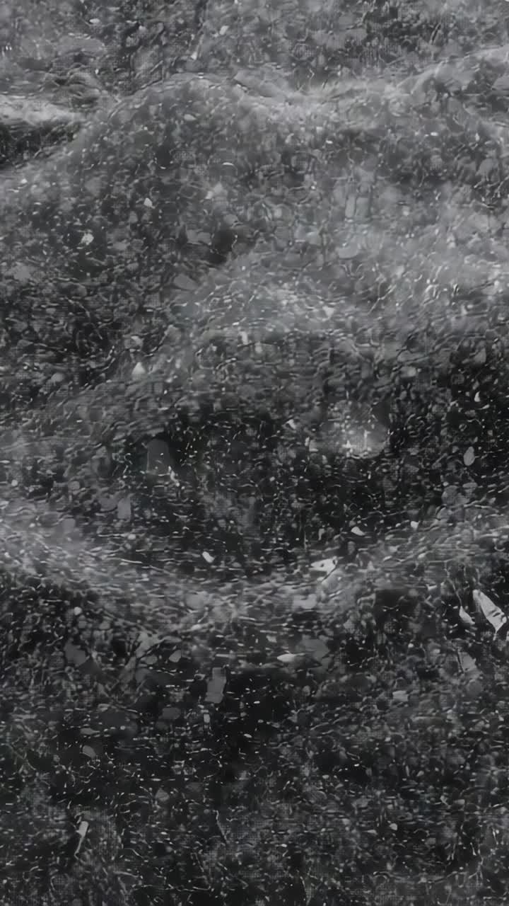 Vertical video: Falling particles striking churning water close-up in spray causing foam and debris