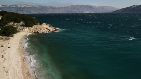 aerial plane of drone with panning to the right showing the beach of baska in croatia in the adriatic sea on a beautiful day on the horizon you can see the great mountains that surround it