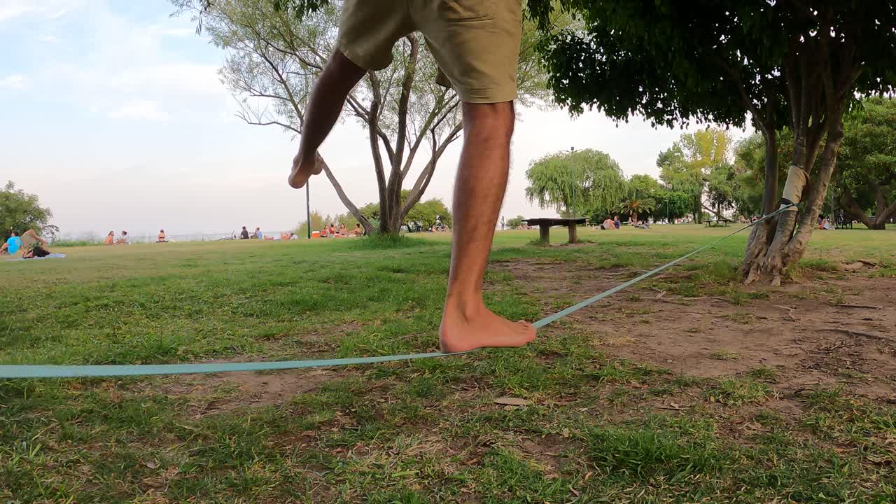 cierra las piernas balanceándose en la línea floja en el parque al aire libre entre árboles