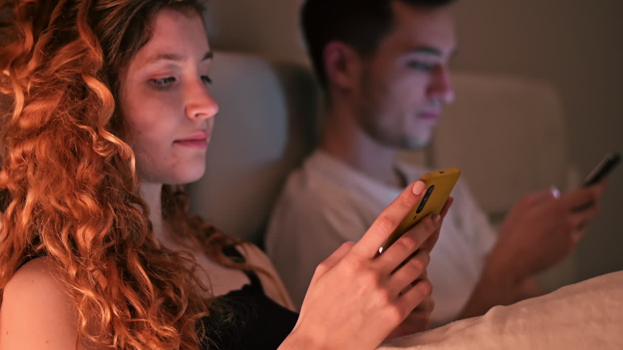 Young couple using smart phones at night in the bed. Colorful light