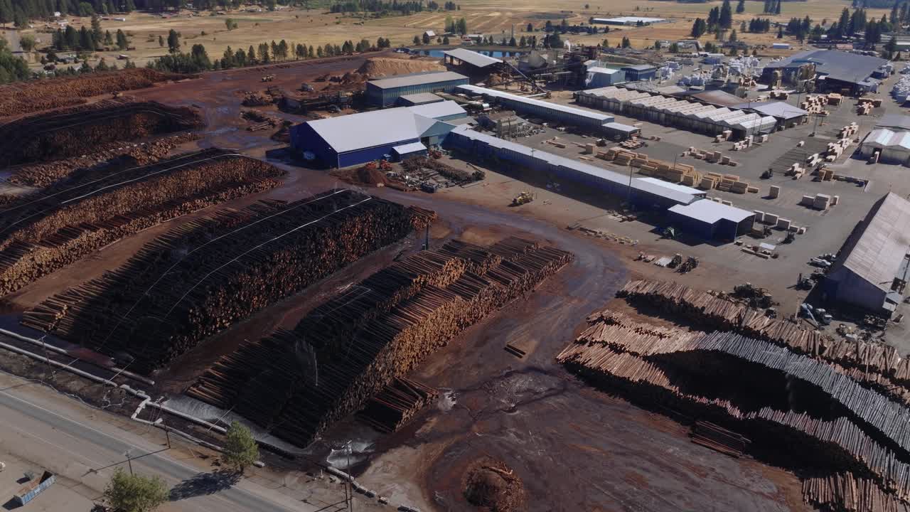 Aerial view of an industrial sawmill with large log stacks outdoors