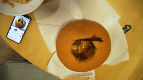 top-down shot of pumpkin ant phone with a carved pumpkin picture on the table, pumpkin in the carving process for halloween