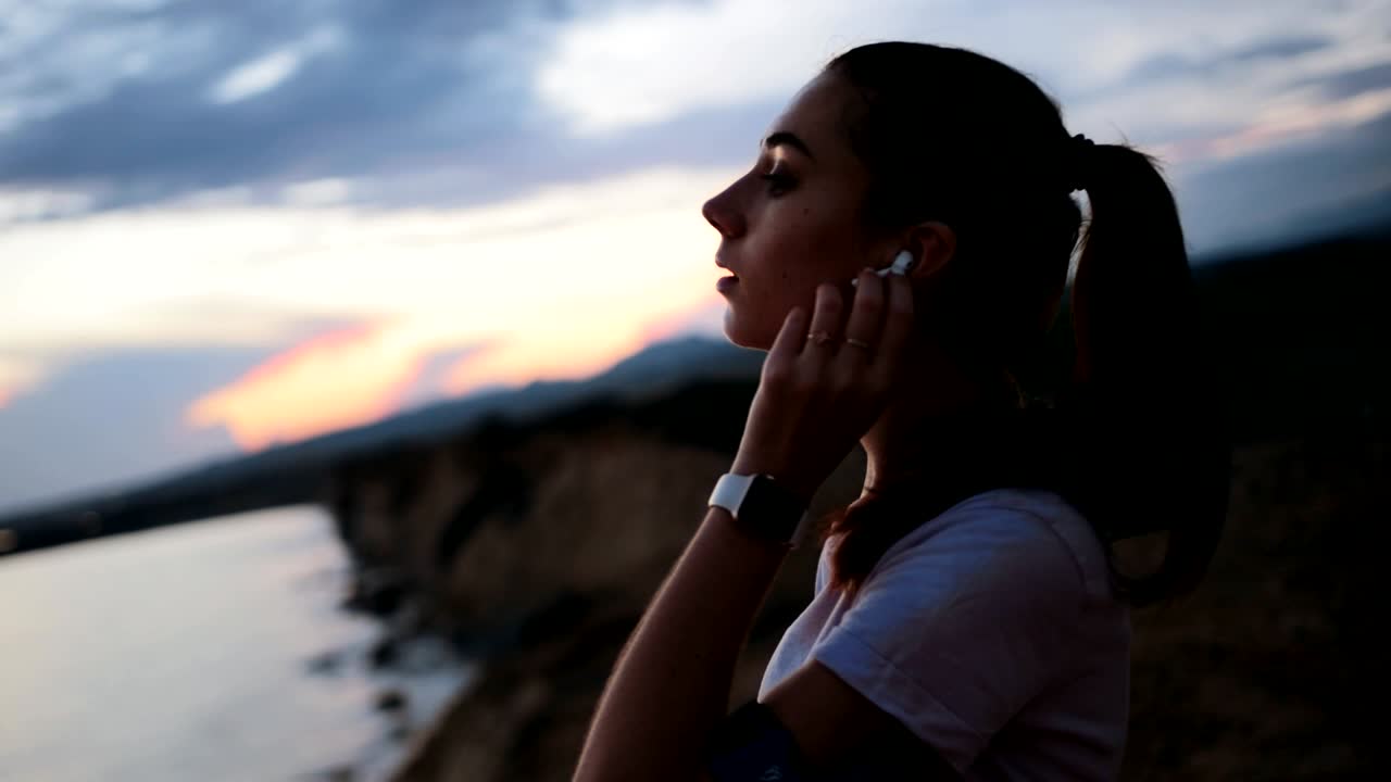 joven corredora relajándose con música en la playa al atardecer
