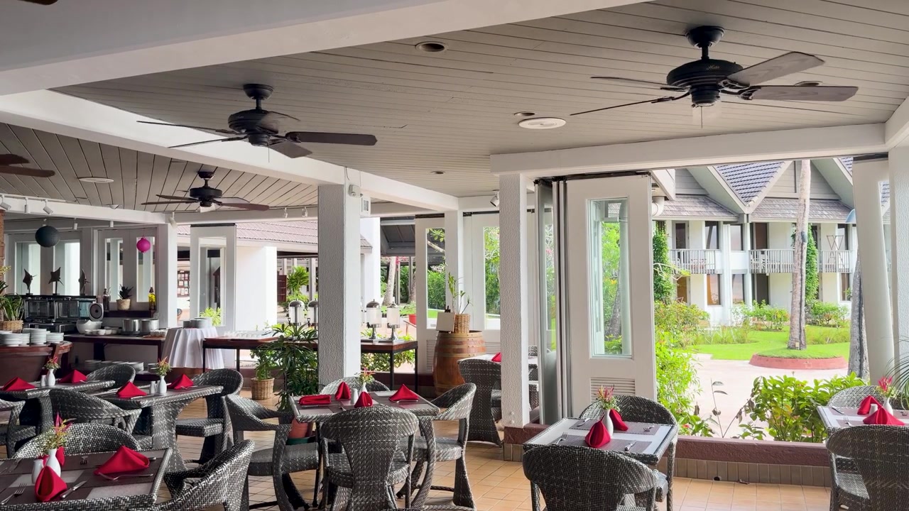 Inquadratura ampia statica di un patio vuoto di un ristorante di un resort tropicale con ventilatori a soffitto che girano