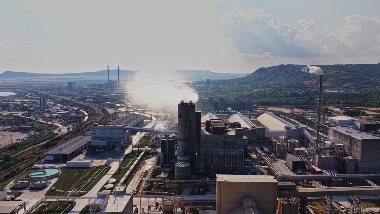 Smoke rises from industrial facility near hills in afternoon light