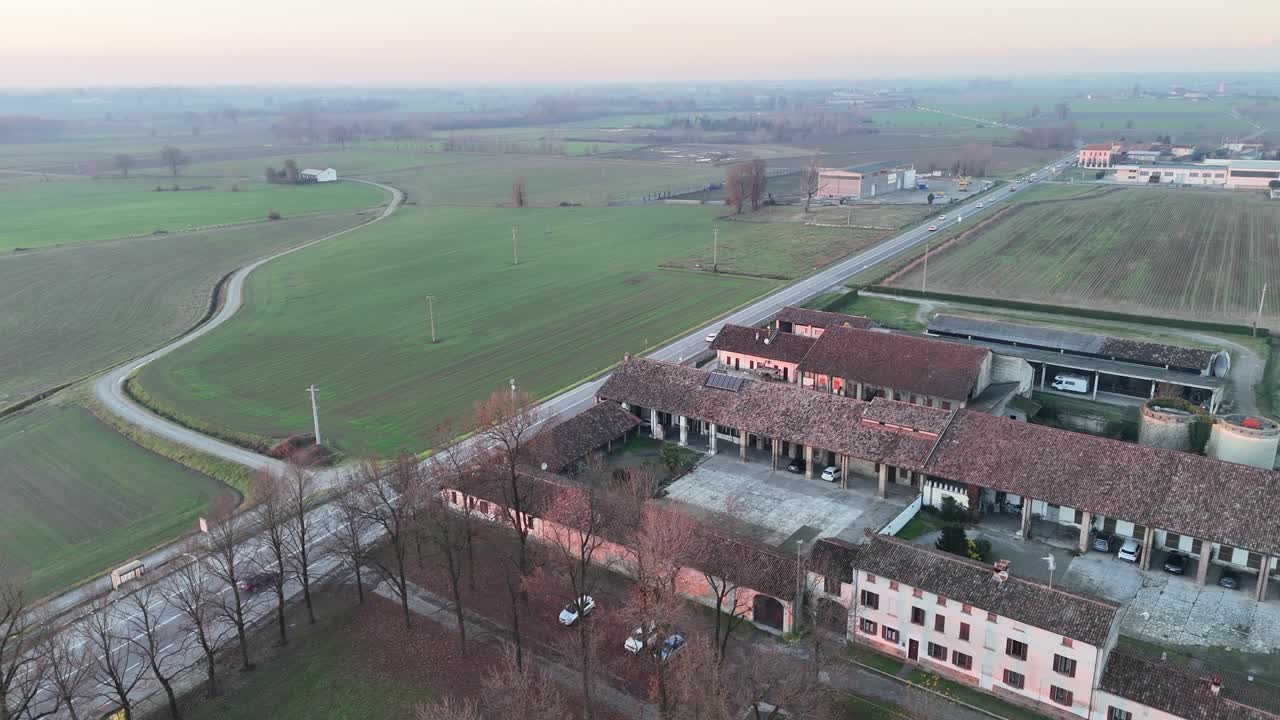 Vista aerea del Santuario della Beata Vergine della Misericordia accanto alla Strada Paullese Strada Provinciale SP 415 fino alla rotonda di Milano, strada moderna che attraversa i campi rurali lombardi al tramonto