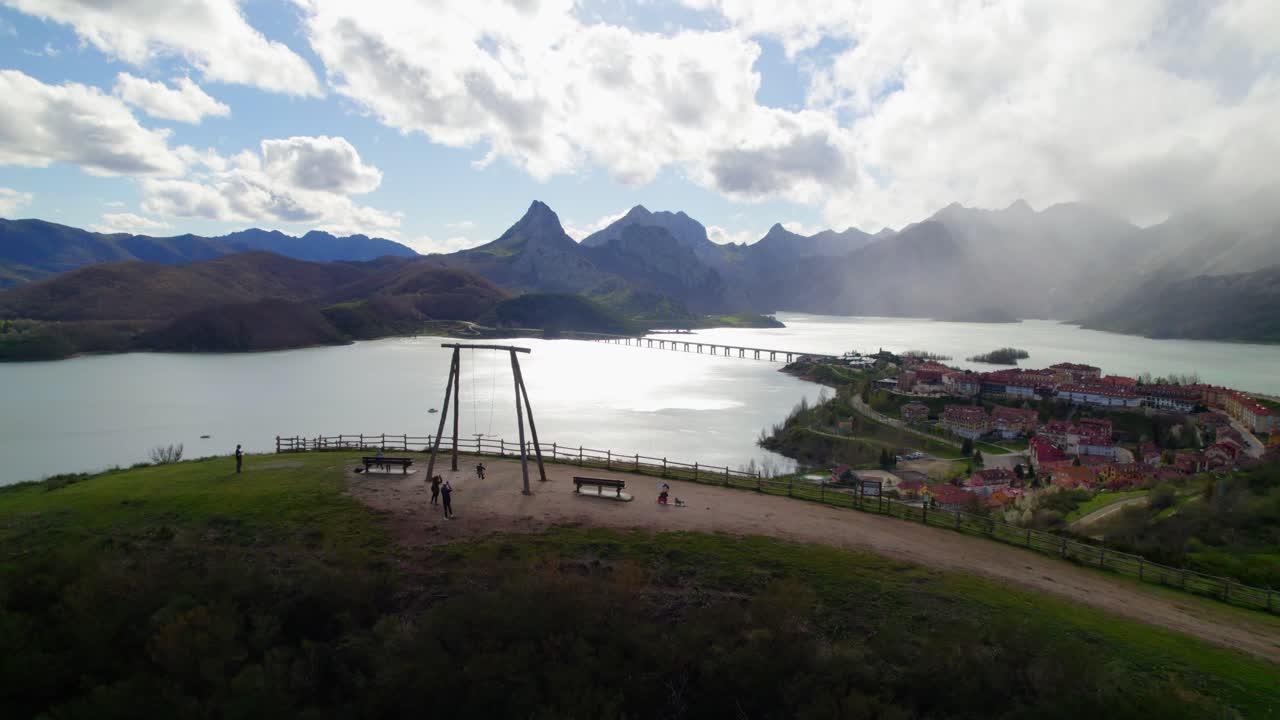 Aerial backward shot of parents swinging their child on the swing at the viewpoint in Ria&ntilde;o, a village in Le&oacute;n, Spain on the shore of a large reservoir in the Cantabrian mountains