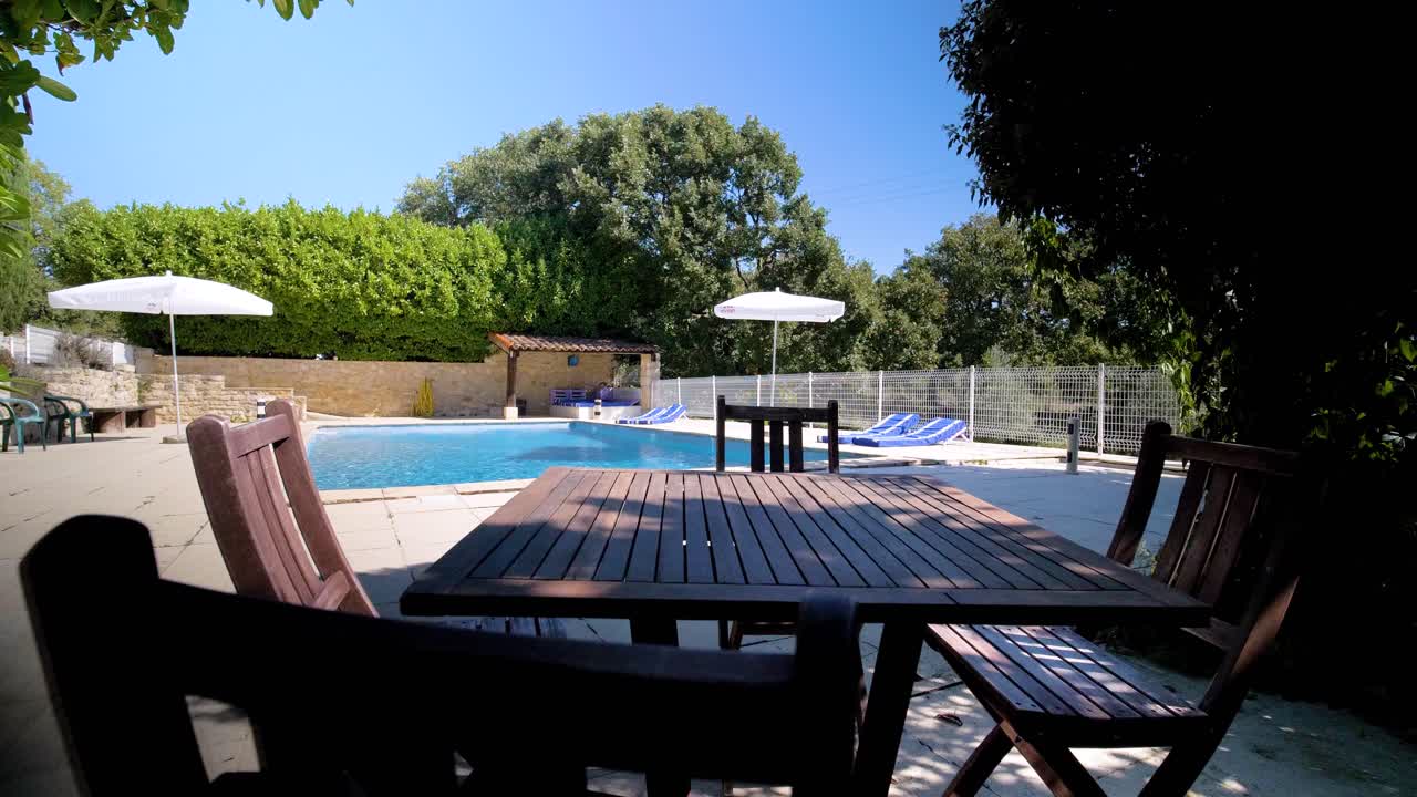 Langsame Einstellungsaufnahme eines Holztisches, der im Schatten neben einem Swimmingpool steht