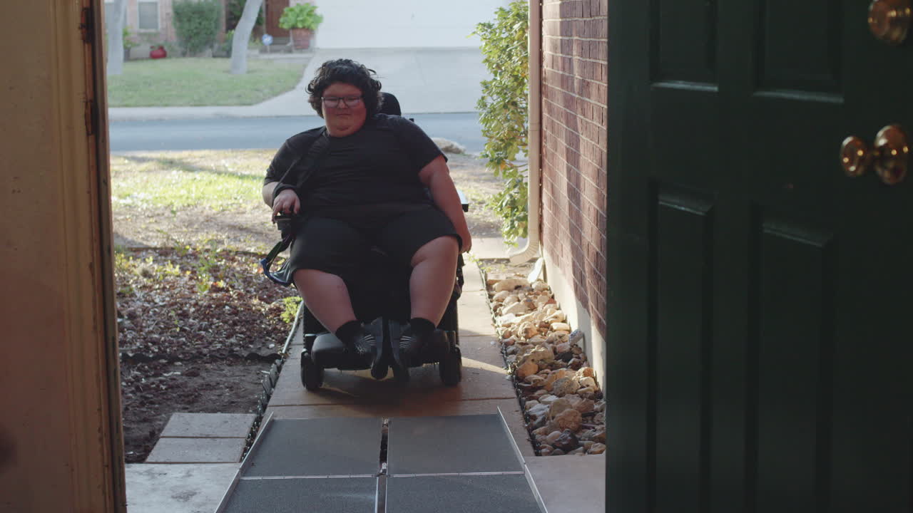 Muscular Dystrophy adolecsent in wheelchair approaches handicap ramp into house