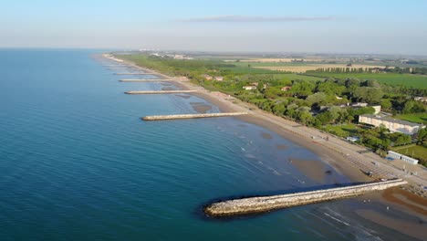 Toma-Aérea-De-La-Pintoresca-Costa-Italiana-Con-Playa-Poco-Profunda-Y-Estructuras-De-Rompeolas-Hechas-Por-El-Hombre