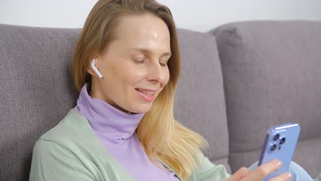 hermosa mujer blanca disfrutando de la música y comunicándose en línea con un teléfono inteligente moderno. mujer bonita de 40 años escuchando canciones favoritas en auriculares inalámbricos y escribiendo mensajes en la aplicación de redes sociales en el teléfono