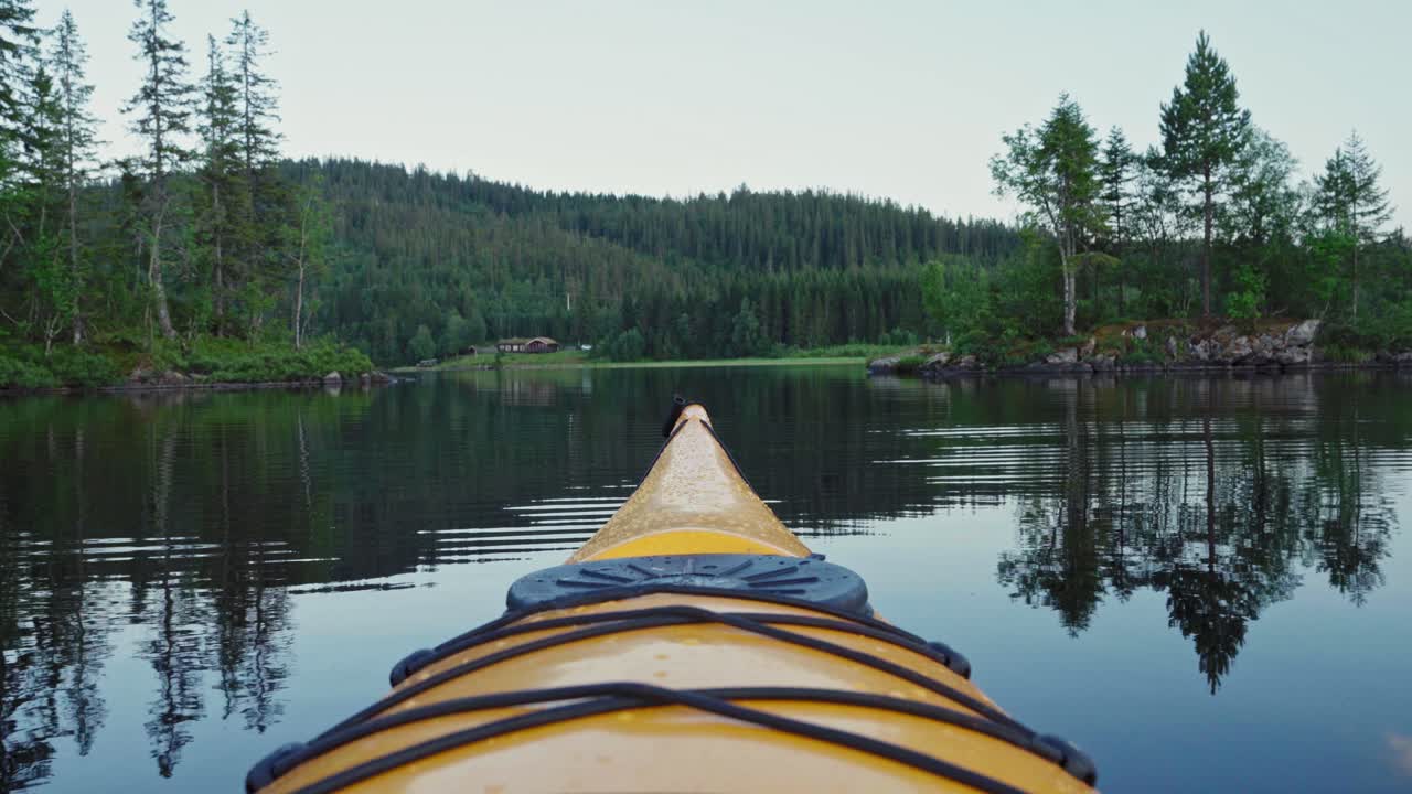 Tip Of Yellow Kayak Floating In Lake With Forested Mountain In Background In Norway