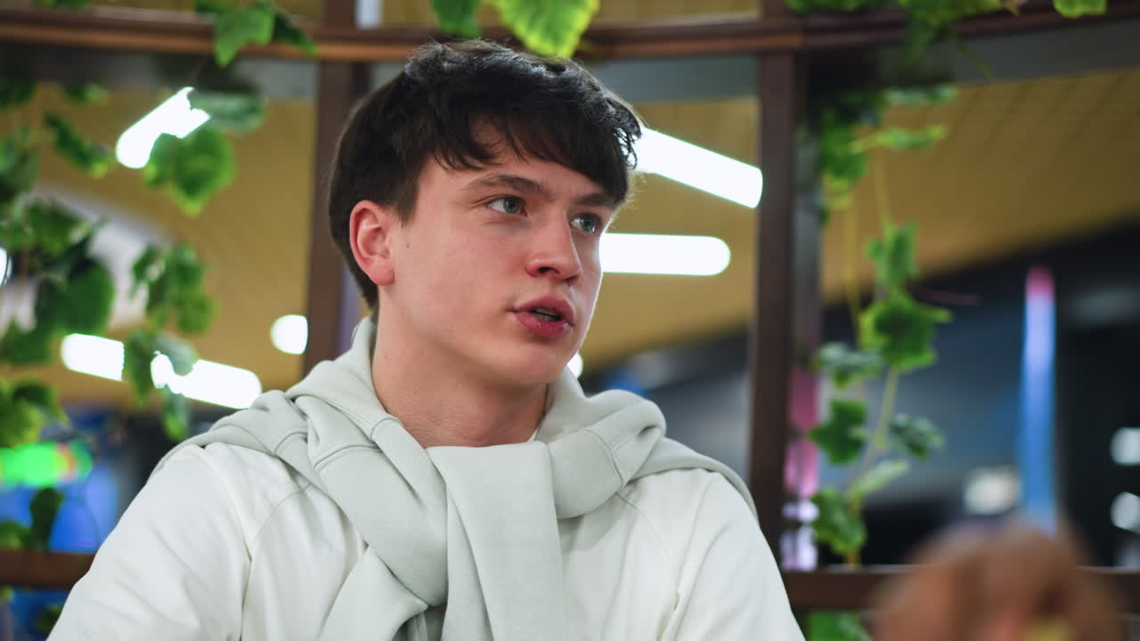 white man swallowing bite while conversing with companion, warm radiance from background creating soft halo glow, closeup on mouth and eyes showing engagement and connection in casual indoor setting