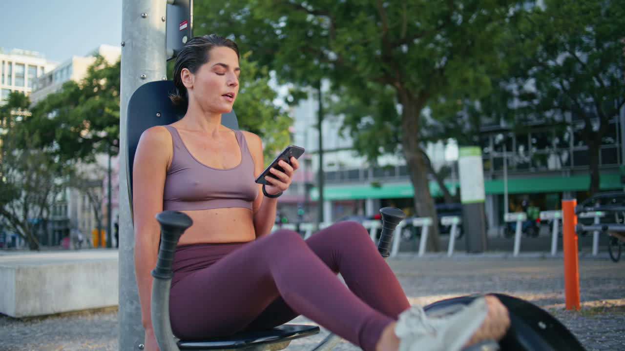 mujer deportiva viendo el teléfono móvil girando los pedales de la máquina de ejercicio en el gimnasio del parque