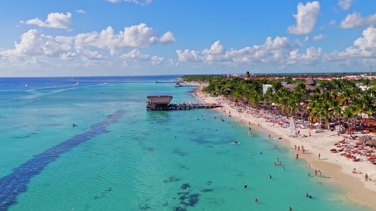 Hermosa playa tropical con turistas nadando en aguas turquesas. Día soleado en un resort caribeño en Bayahibe, República Dominicana. Vista aérea hacia adelante