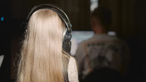 niña canta en el micrófono con el maestro. niña rubia se para frente al tutor mientras practica la voz en el estudio de grabación. niña talentosa