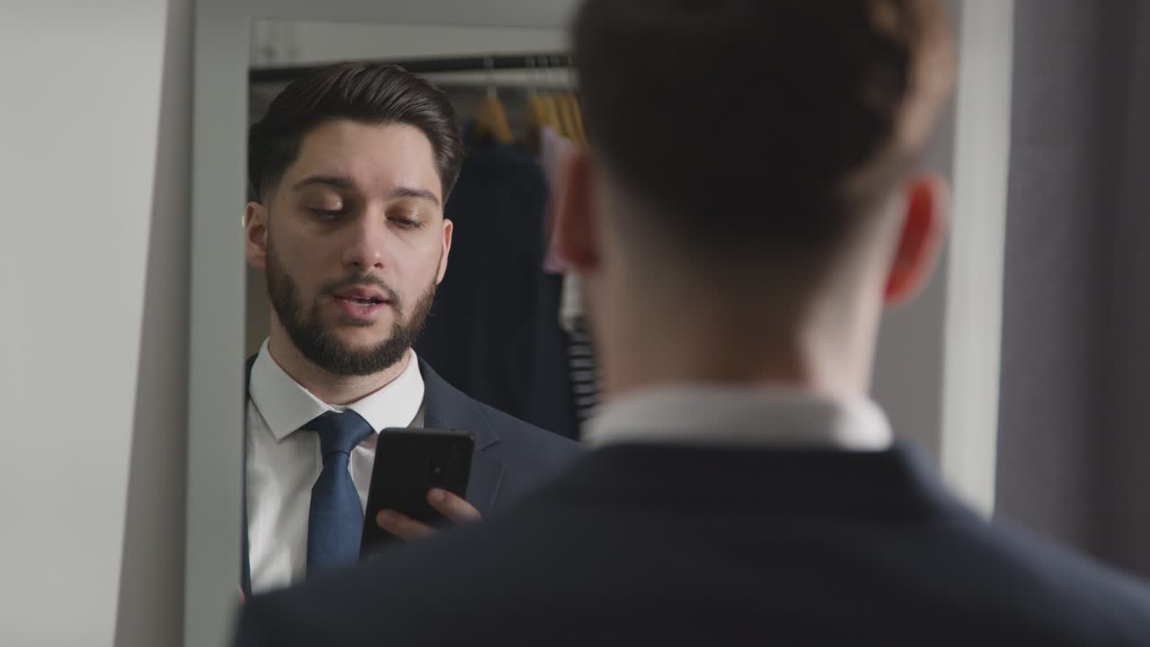 Young Man In Suit At Home Practising Job Interview Technique Reflected In Mirror Using Mobile Phone